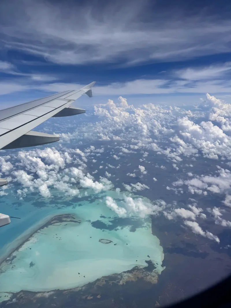 View of a turquoise lagoon and clouds from an airplane window on a flight over tropical islands