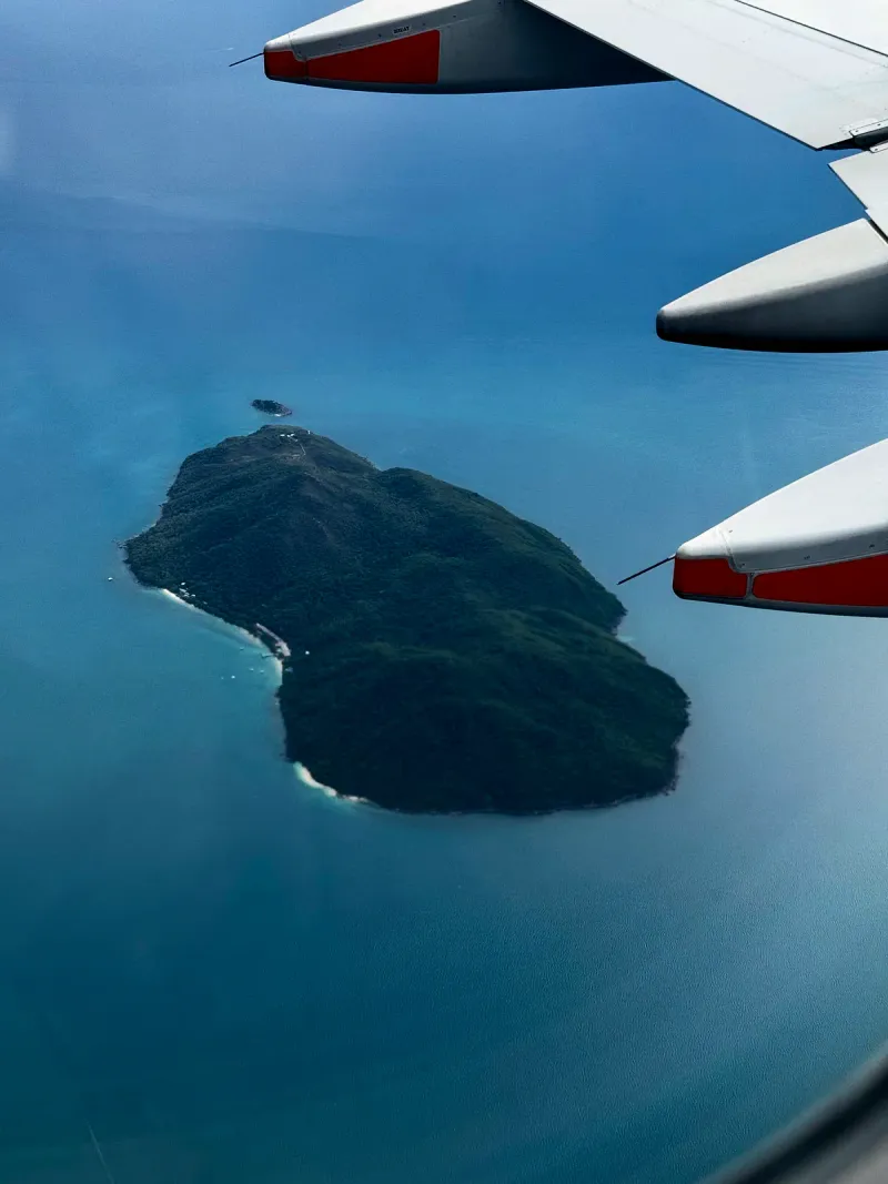 旅客機の翼の向こうに見える、深い青の海に囲まれた、森に覆われた島