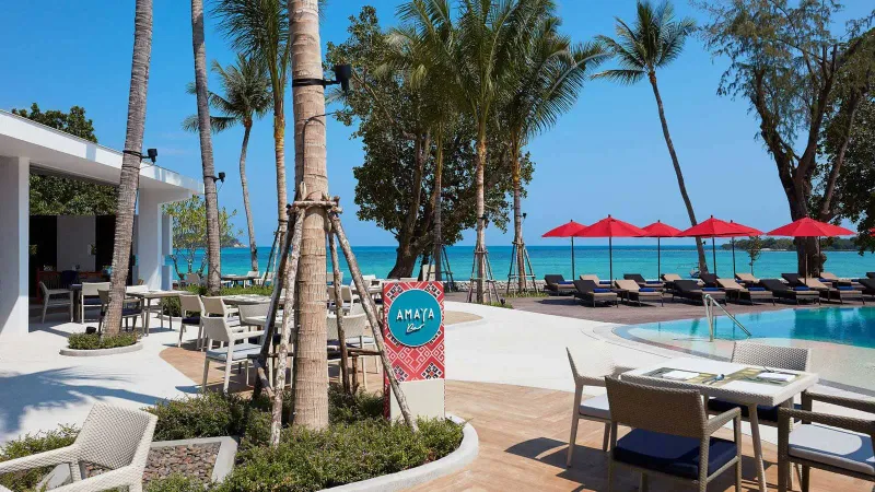 Amaya beach eatery terrace at Amari Koh Samui with tables by the pool and red umbrellas on the sand