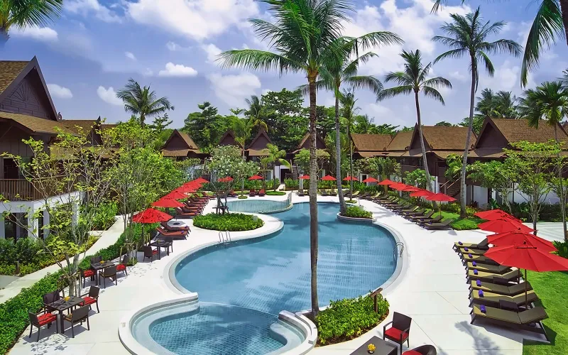 Curving Amari Koh Samui pool with red umbrellas, sunbeds and coconut palms in front of the guest wings