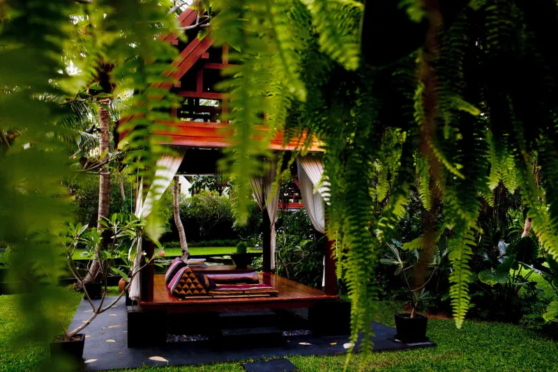 Thai-style timber sala with cushions seen through ferns in the gardens of Anantara Bophut Koh Samui