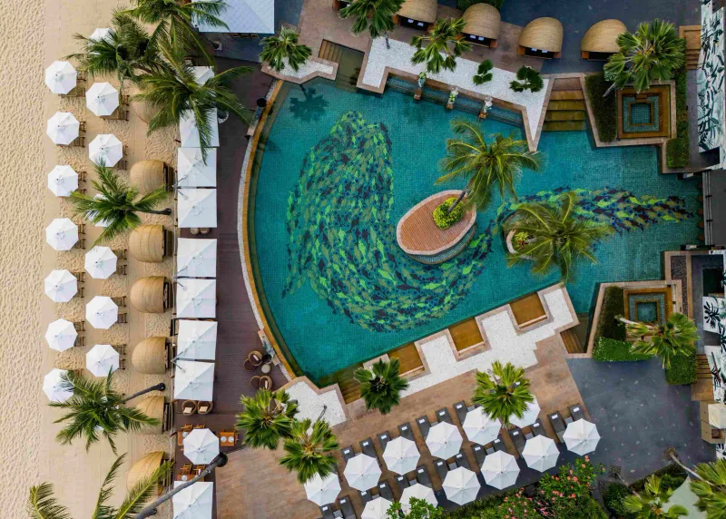 Aerial view of the curved Anantara Bophut pool with fish mosaic, sun umbrellas and cabanas beside the beach