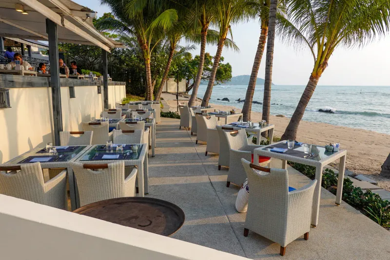 Beachfront restaurant terrace at Anantara Lawana with tables, white chairs and palms above the sea