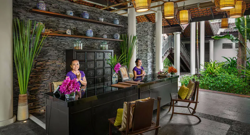 Spa reception desk with stone wall, Thai lanterns and two staff members at Anantara Lawana