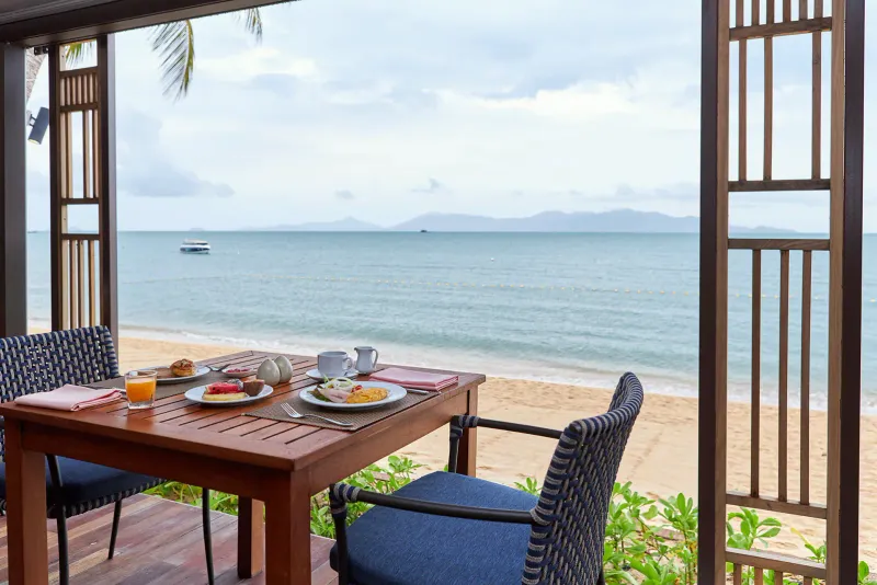 Breakfast table set with fruit, an omelette and orange juice facing the beach at Bandara Resort Samui