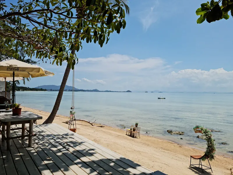 A hidden roadside bar's plastic chairs and umbrella facing the water at Bang Makham
