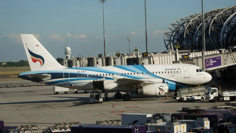 Bangkok Airways Airbus A319 at a Suvarnabhumi Airport gate with ground vehicles around it