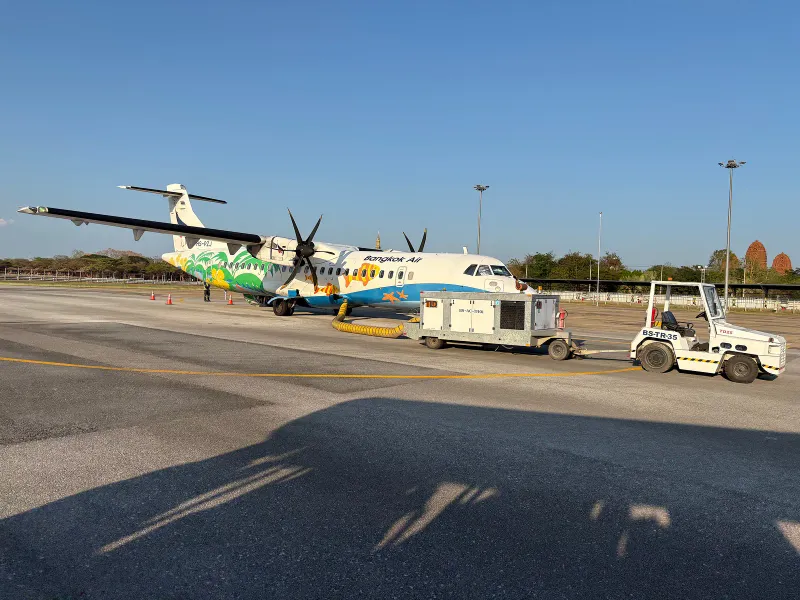 Bangkok Airways ATR turboprop in colourful livery parked on an airport apron with a ground power unit