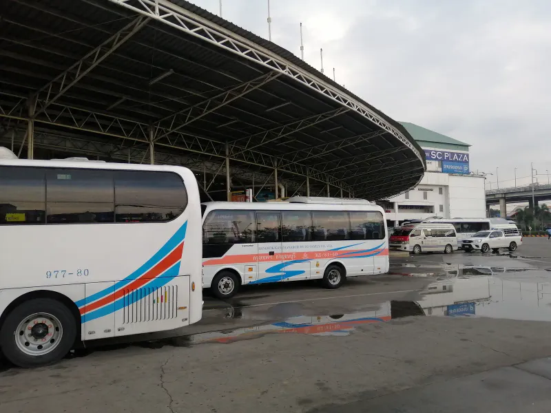 Coaches and minibuses parked under a large covered bay at a Bangkok bus station