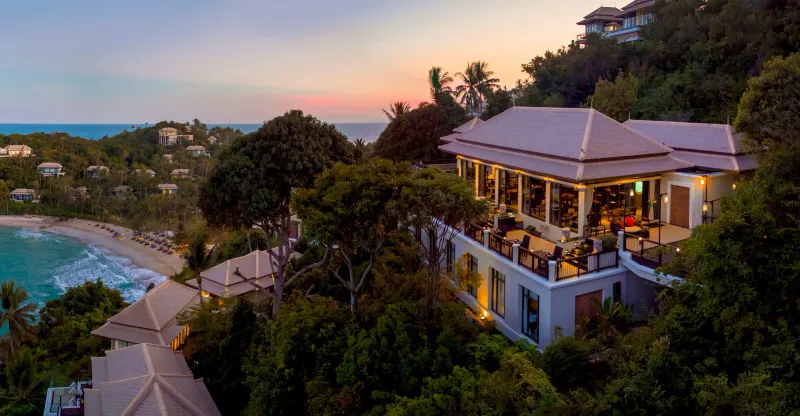 Banyan Tree Samui hillside at sunset with lit restaurant terraces above the bay and scattered villas