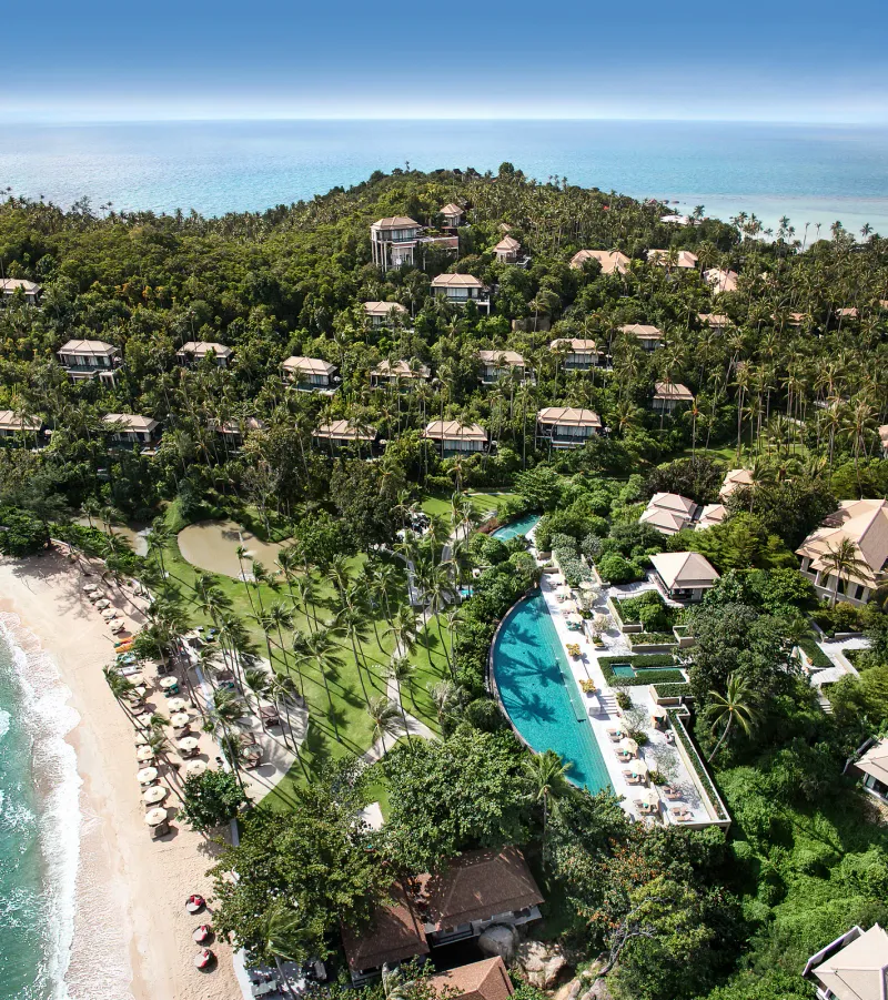 Aerial view of Banyan Tree Samui with its curved pool, lawns, beach loungers and villas climbing the hillside