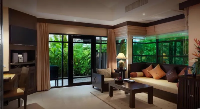 Living area of a Bo Phut Resort and Spa villa with sofas, cushions and sliding glass doors onto the garden