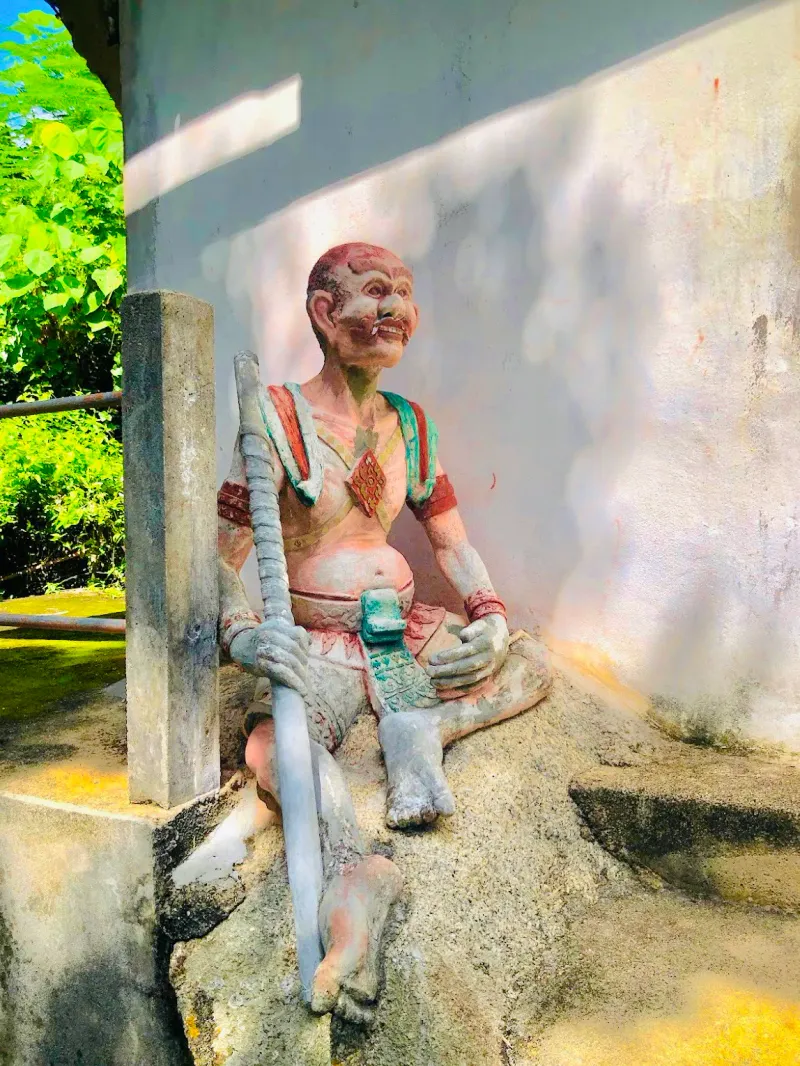 Weathered painted guardian statue seated at the corner of the shrine building