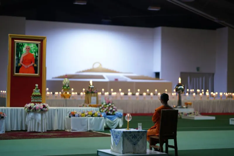 Mönch sitzt zwischen Kerzen und Opfergaben während einer buddhistischen Zeremonie an einem Feiertag in einem thailändischen Tempel