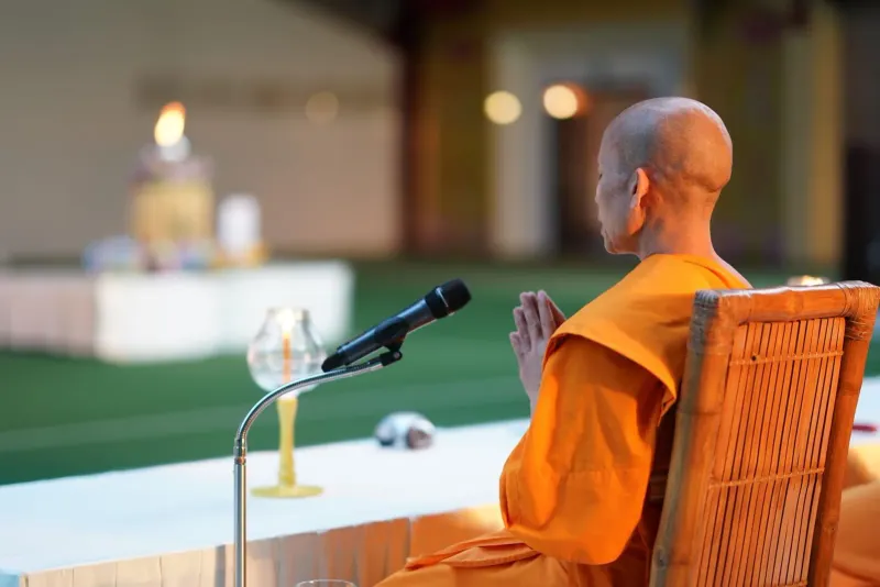 Buddhistischer Mönch in safranfarbenen Roben sitzt in einer Tempelhalle während einer Feiertagszeremonie auf Koh Samui