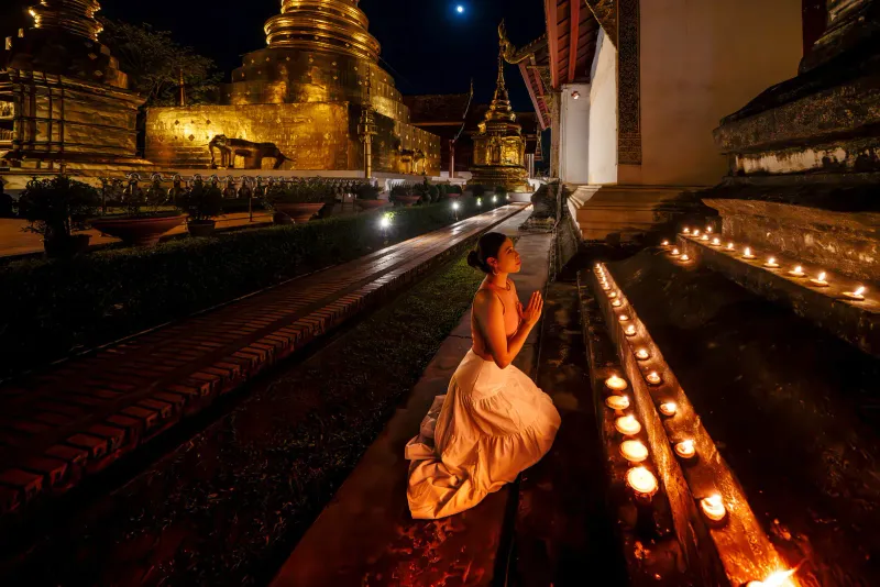 A woman kneeling among candles at a temple after dark