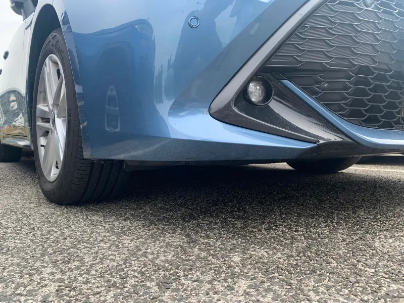 Close-up of a blue car front bumper and wheel arch at ground level