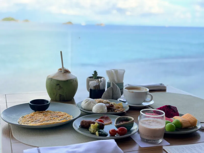Breakfast table with omelette, dim sum, fruit and coconut above the sea at Conrad Koh Samui