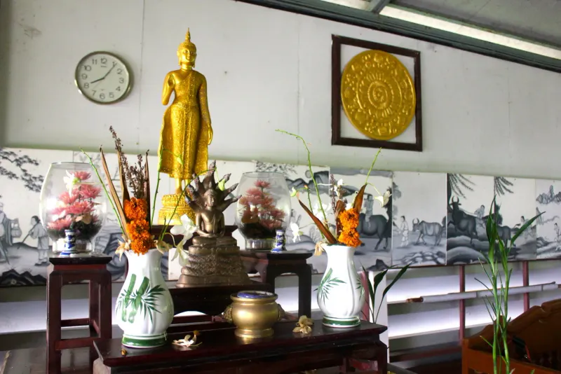 Golden standing Buddha statue on an altar with flower vases and Chinese calligraphy scrolls behind