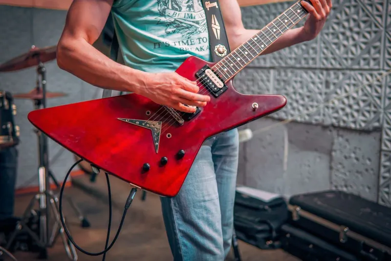 Musiker spielt E-Gitarre, im Hintergrund ein aufgebautes Schlagzeug, die Art von Backline, die ein Proberaum bereitstellt