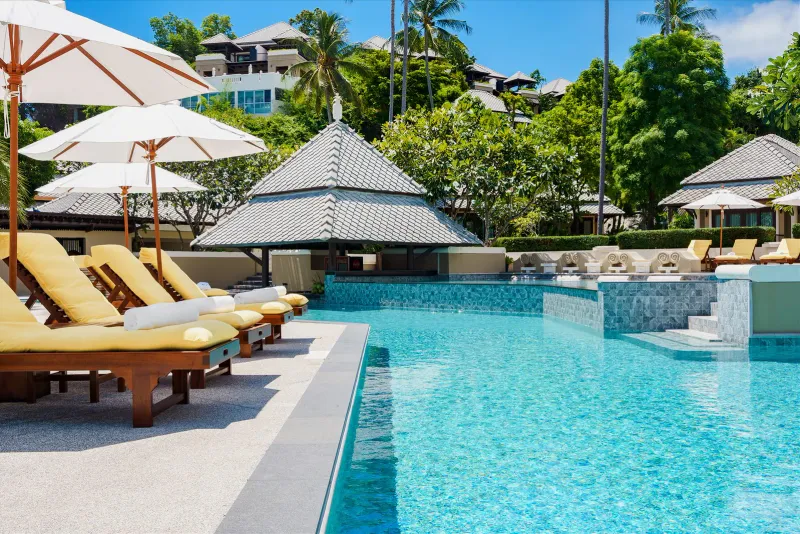 Fair House Villas & Spa pool with yellow-cushioned loungers and the swim-up bar pavilion under a hillside of villas
