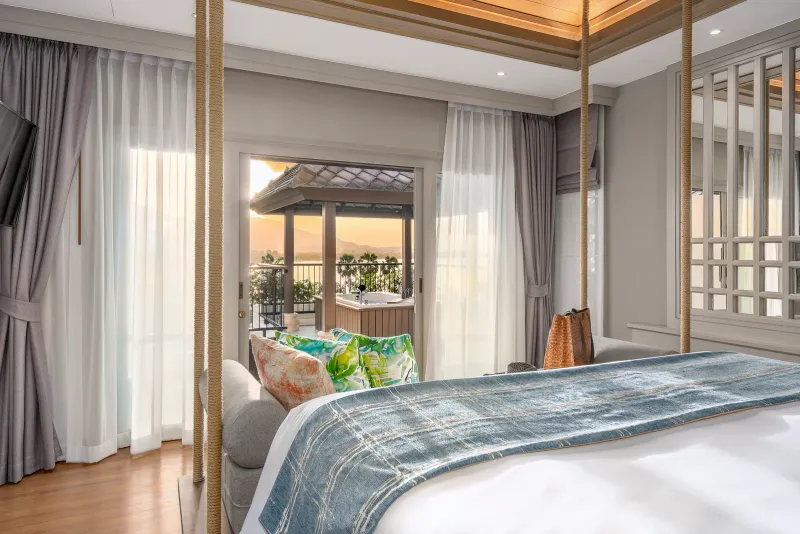 Suite bedroom with rope-hung canopy bed and a terrace jacuzzi looking over the bay at sunset