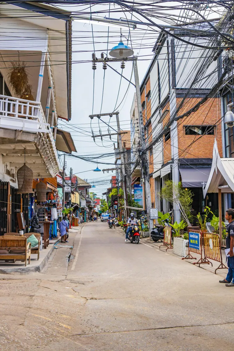 Narrow street in Fisherman's Village Bophut with shops, motorbikes and overhead cables on Koh Samui
