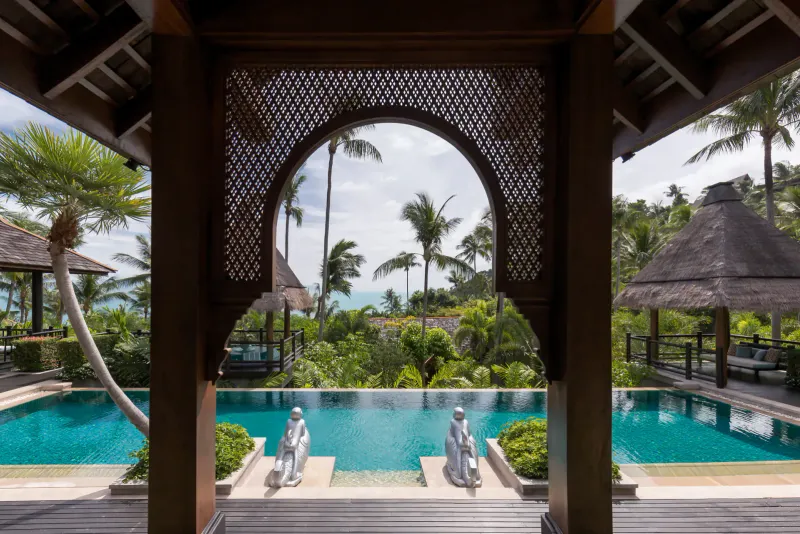 Carved arch pavilion framing a villa infinity pool and the hillside at Four Seasons Resort Koh Samui