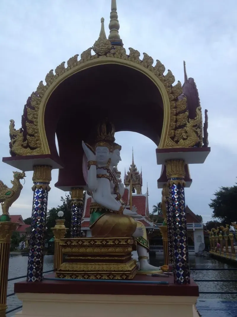 A many-armed deity statue beneath an ornate archway at nearby Wat Plai Laem
