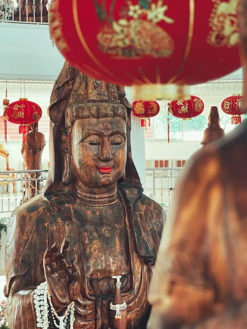 Serene Guan Yin statue amid vibrant red lanterns in a Thai temple