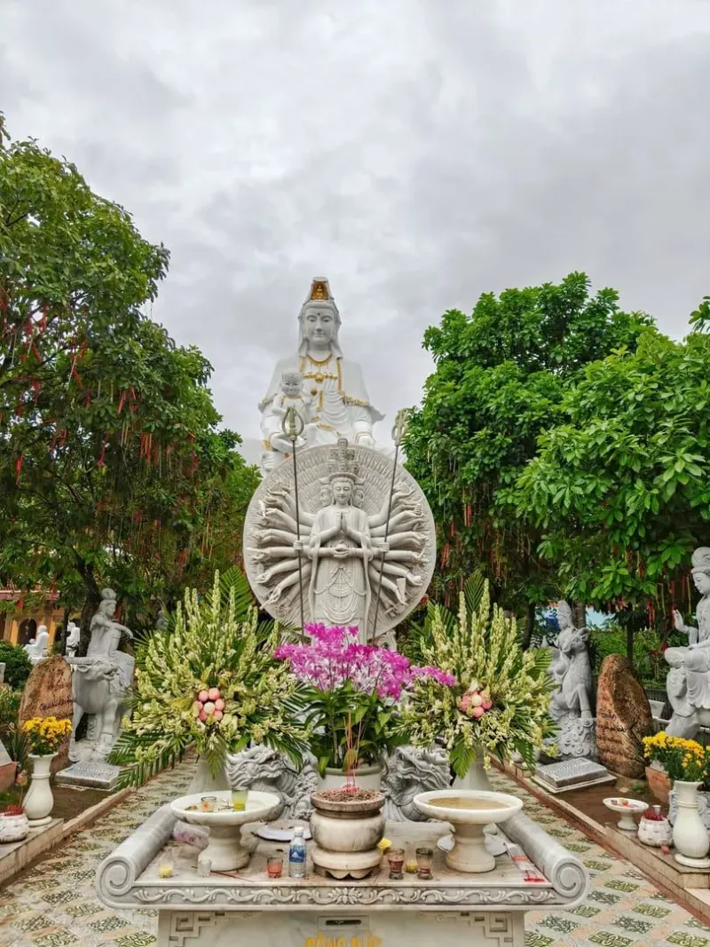 A serene statue of Guan Yin surrounded by vibrant greenery and flowers in Bình Ninh, Việt Nam