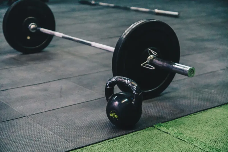 Barbell and kettlebell resting on a gym floor, the conditioning equipment BXB Fight Lab lists on its facilities page