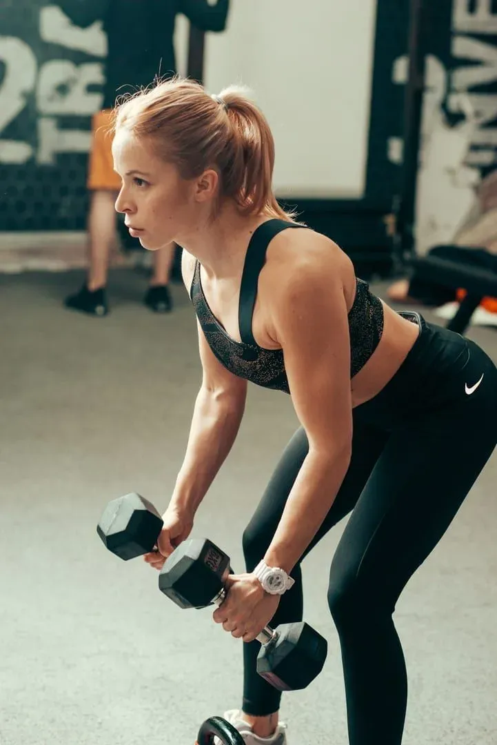 Woman lifting dumbbells with proper form in a modern gym, part of the strength and conditioning scene on Koh Samui