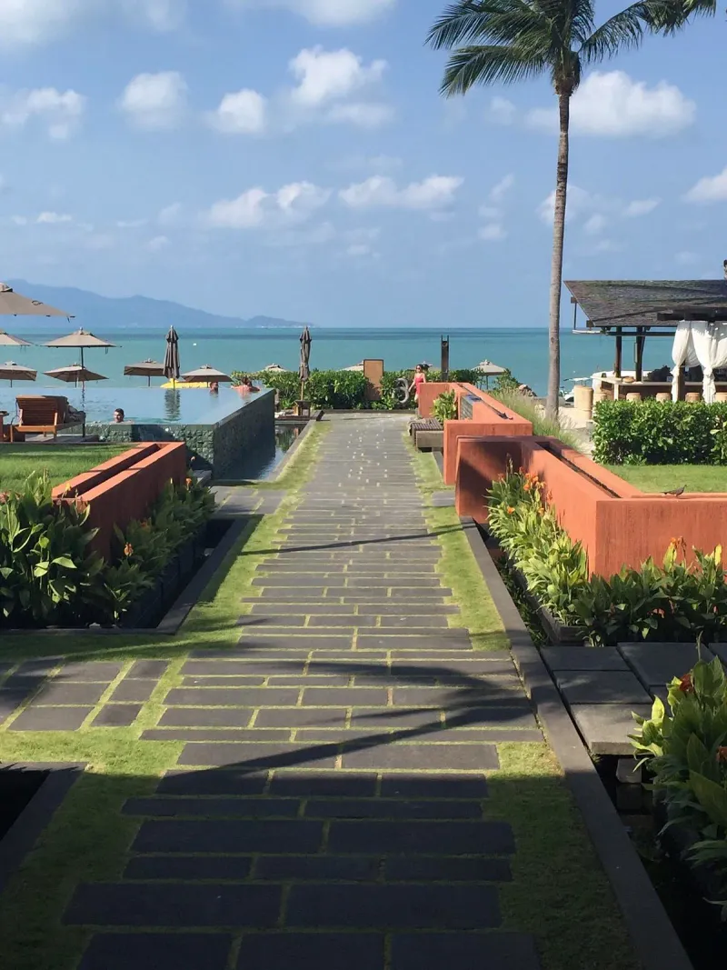 Stone path between landscaped terracotta walls leading to the Hansar Samui pool and the sea