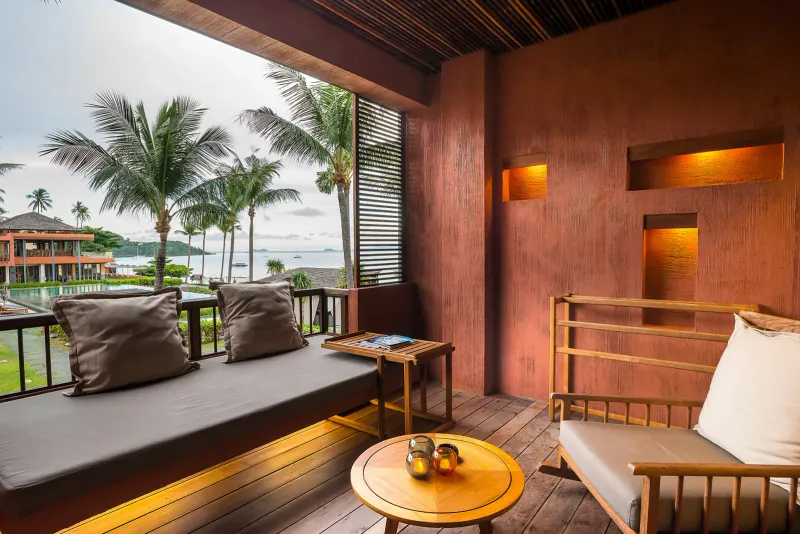 Balcony daybed at Hansar Samui with cushions, wooden screens and palm trees above the bay