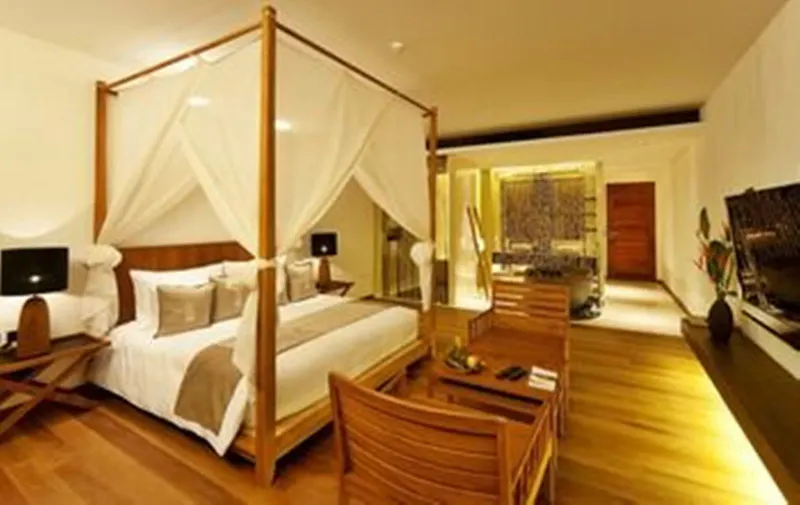 Hansar Samui room with a canopy bed, armchairs and a wooden floor leading to the bathroom
