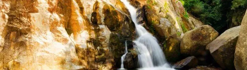 Wide view of water threading down Hin Lad's granite rock face