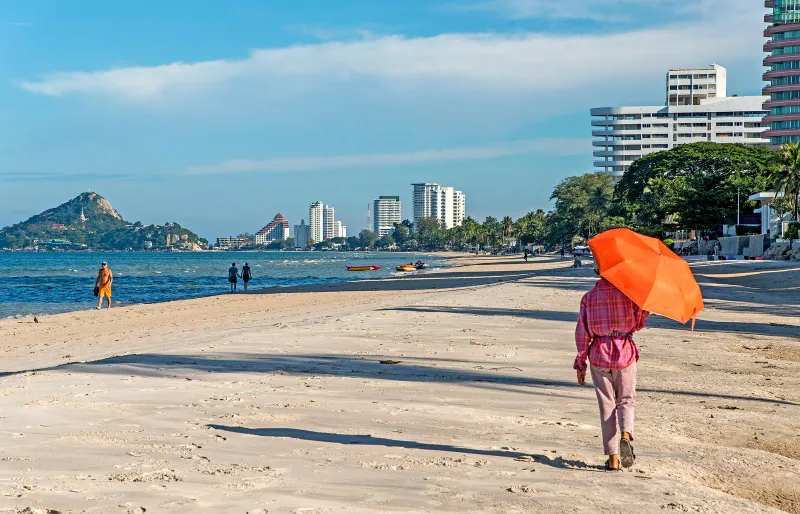 Long sandy beach at Hua Hin with a walker, hills and apartment towers in the distance