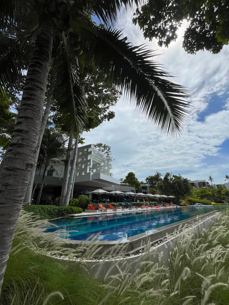Long lap pool at Hyatt Regency Koh Samui with orange loungers, striped umbrellas and a yellow slide in the distance