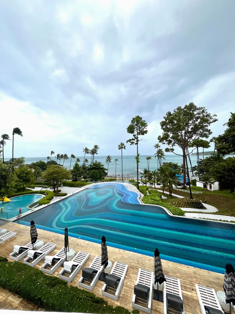 View from an upper level over the mosaic-tiled pool, loungers and palm trees to the sea at Hyatt Regency Koh Samui