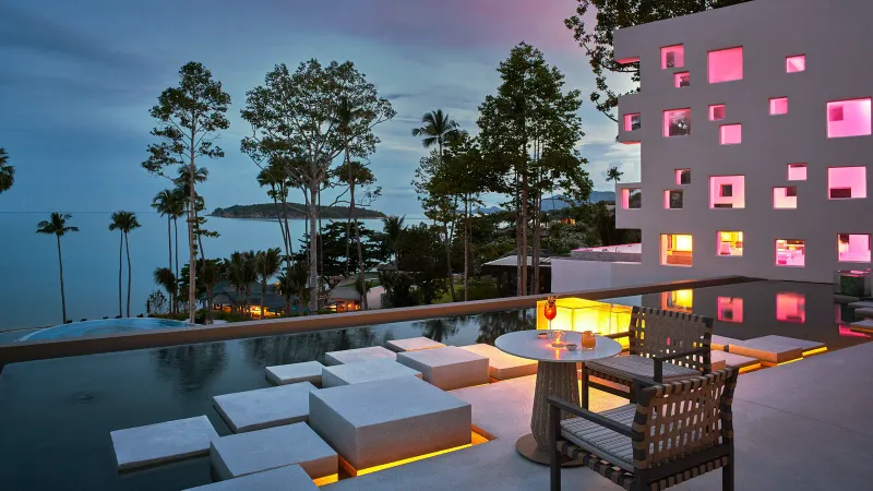 Dusk terrace at Hyatt Regency Koh Samui with stepping-stone seats in a water feature, a cocktail and the lit building behind