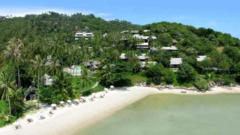 Aerial view of Kamalaya Koh Samui bungalows among palms above its private sandy cove at Laem Set