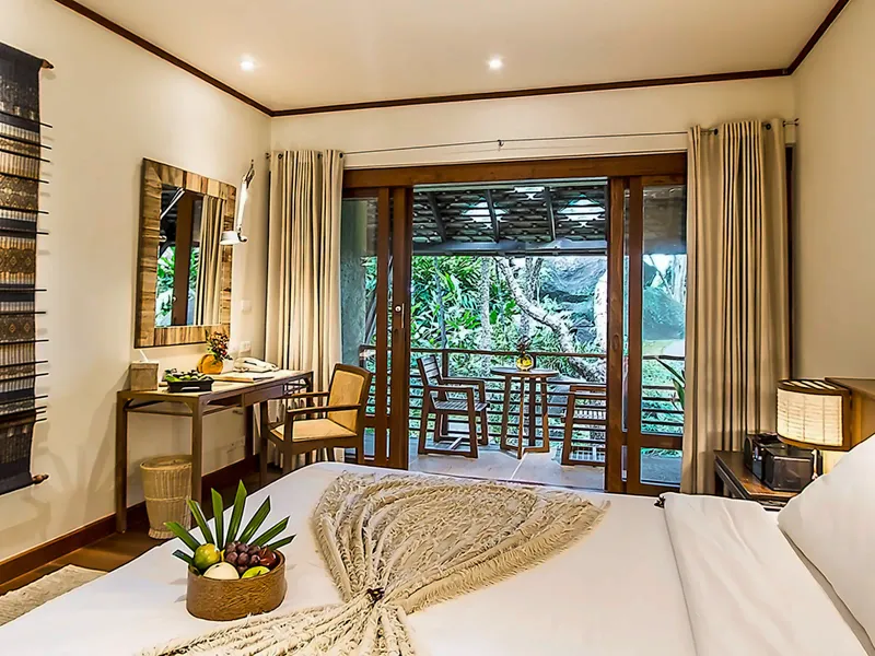 Bedroom at Kamalaya Koh Samui with woven bed runner, teak floor and balcony doors opening to the garden