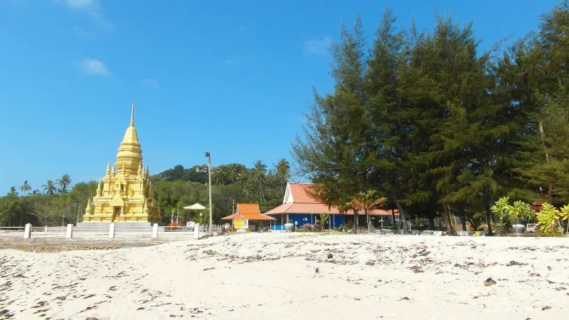 Golden stepped chedi against a blue sky beside palm trees on Koh Samui