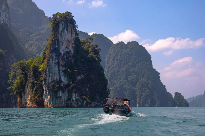 Longtail boat crossing Cheow Lan Lake past limestone karsts in Khao Sok National Park