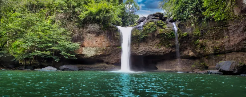 A wide cascade falling into a turquoise jungle pool, illustrating the cooling pools found at Samui's mountain waterfalls