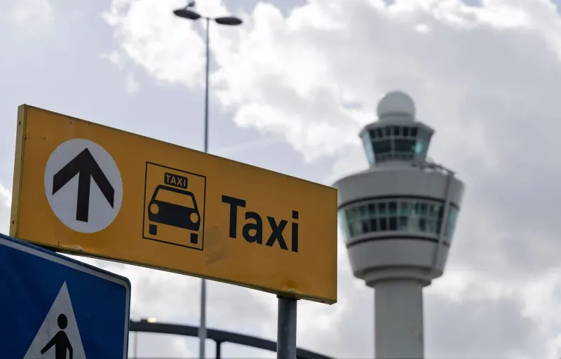 Insegna dei taxi all'aeroporto di Koh Samui con la torre di controllo sullo sfondo, contro un cielo nuvoloso