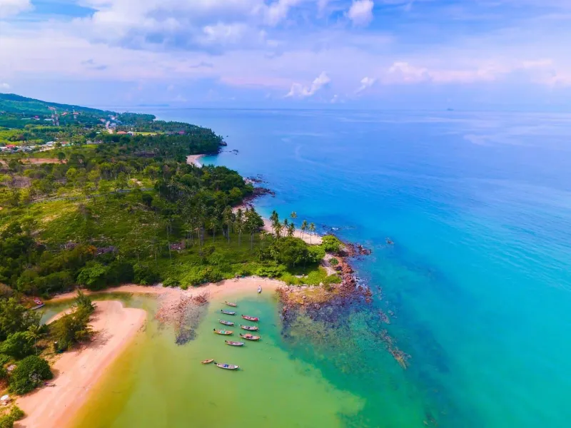 Tropical island coastline with lush greenery and crystal-clear water similar to Koh Samui's quieter west coast