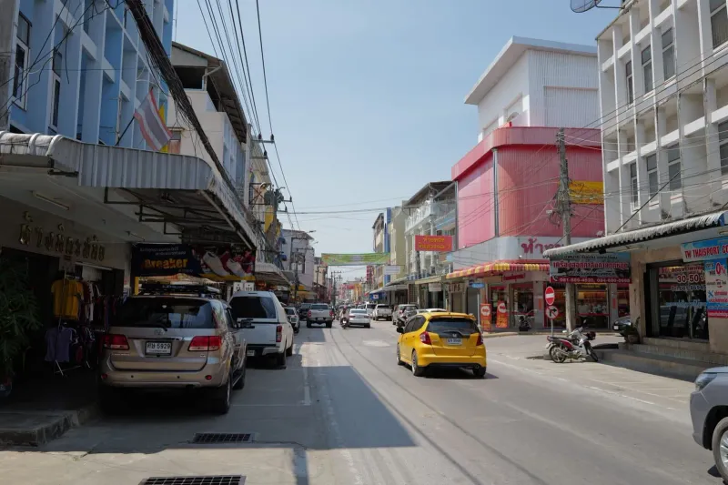 Traffic and colorful storefronts on a Koh Samui town street where local car rental shops operate
