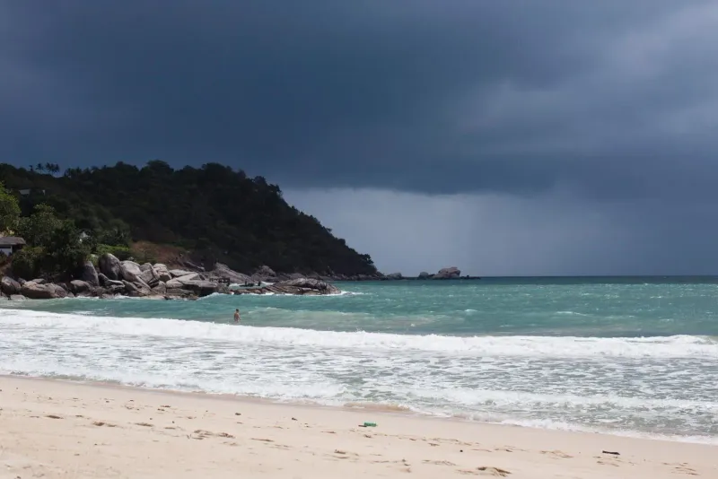 A dark monsoon sky over a beach and headland